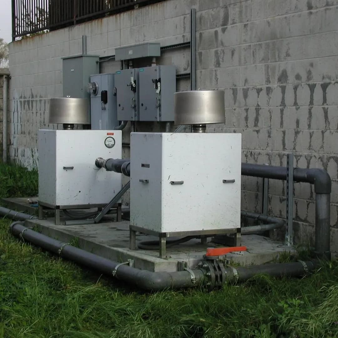 Two white industrial air handling units with stainless steel tops connected by grey piping with a large orange valve.