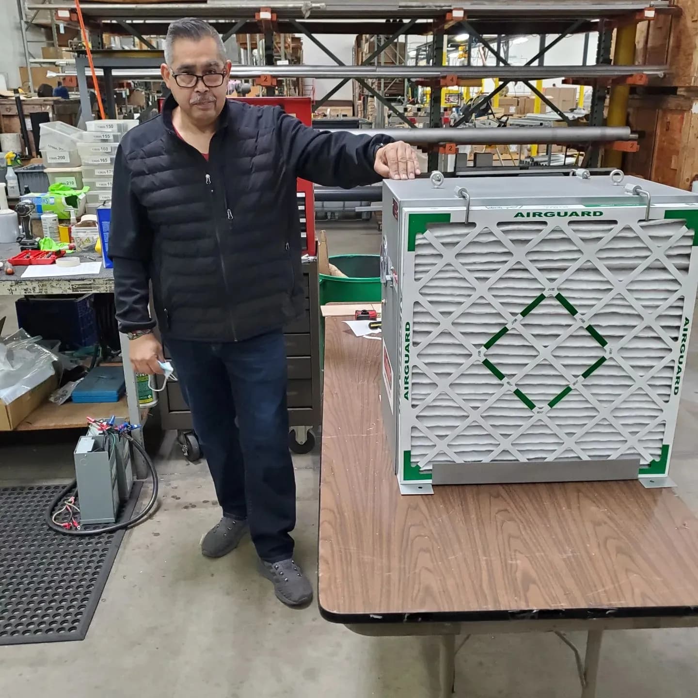 A man in an industrial warehouse resting his hand on a large Airguard industrial air filter unit.